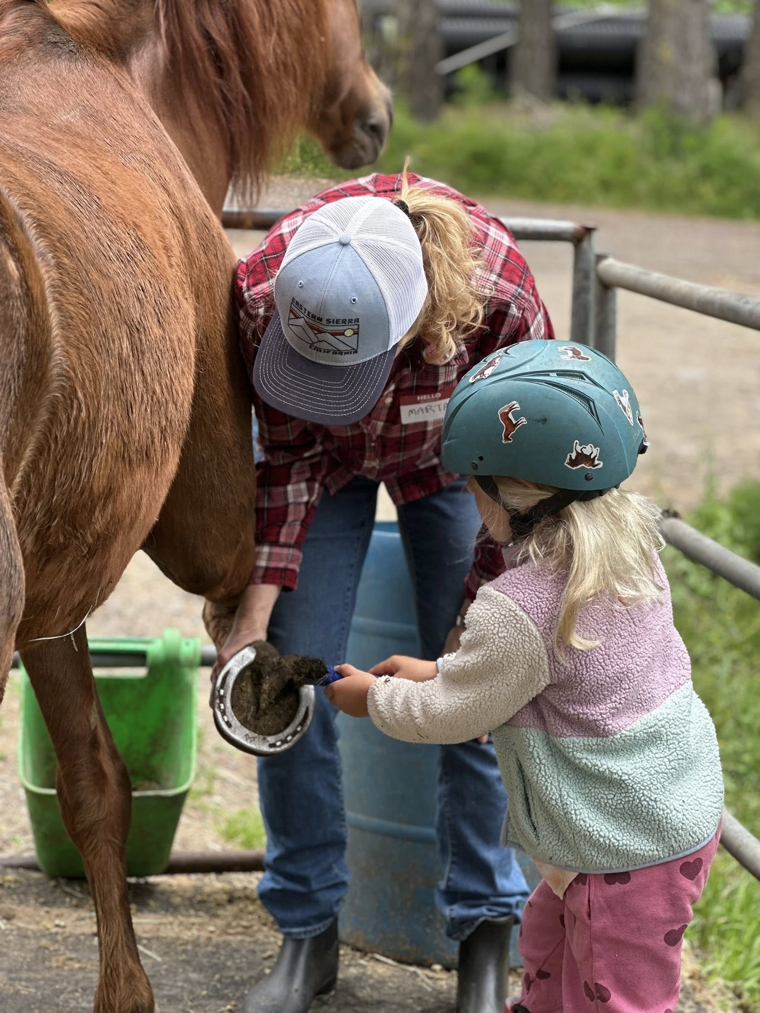 Child learning horse hoof care with instructor